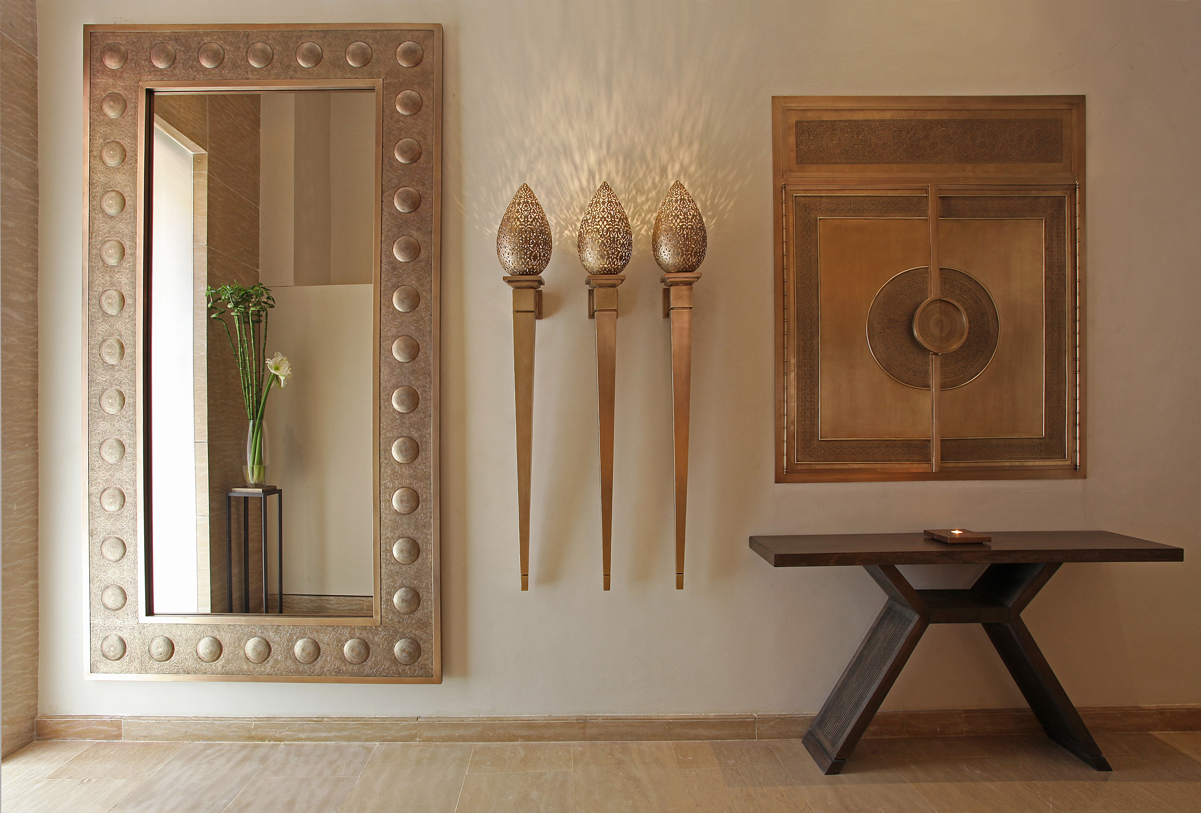 A studded-frame rectangular mirror above a console table, flanked by brass torch sconces in a warm room.